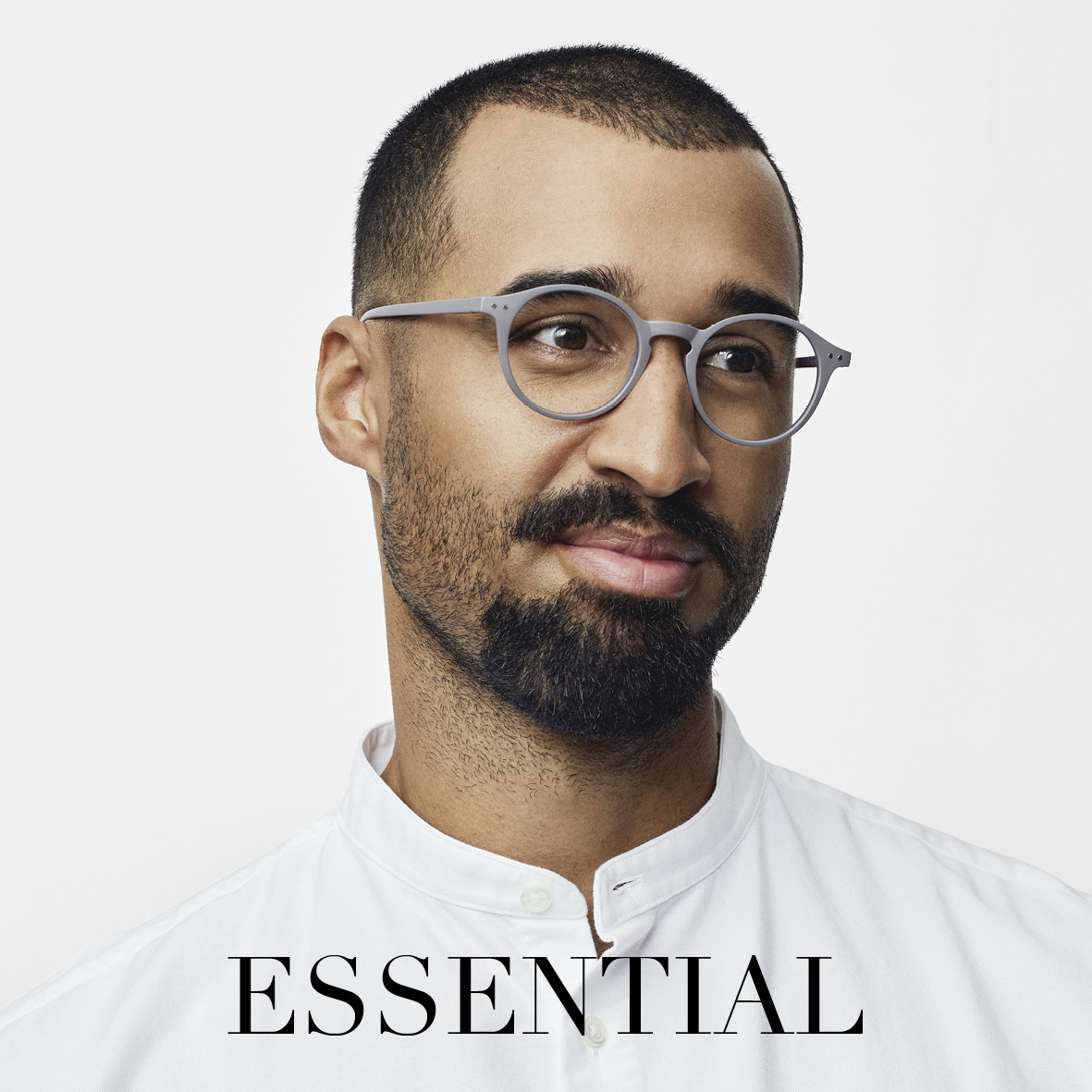 Ein Mann mit kurzen Haaren, einem Bart und einer Brille trägt ein weißes Hemd mit Kragen und lächelt freundlich. Das Wort ESSENTIAL steht in fetten schwarzen Buchstaben am unteren Rand des Bildes.