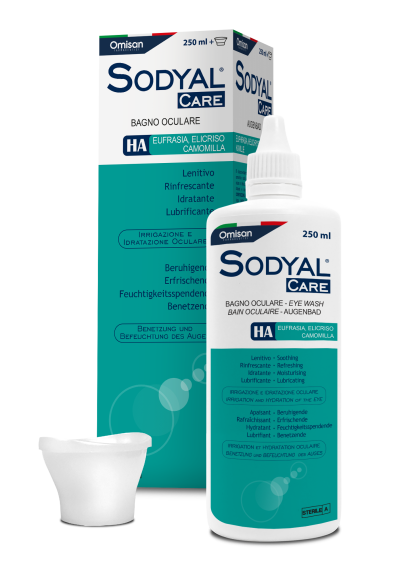 Eine weiße 250-ml-Flasche Sodyal Care Augenspülung mit einem blauen Etikett steht vor der dazugehörigen Schachtel. Neben der Flasche befindet sich ein Augenbecher. Die Verpackung ist mit italienischem Text versehen und hebt Inhaltsstoffe wie Kamille und HA hervor.