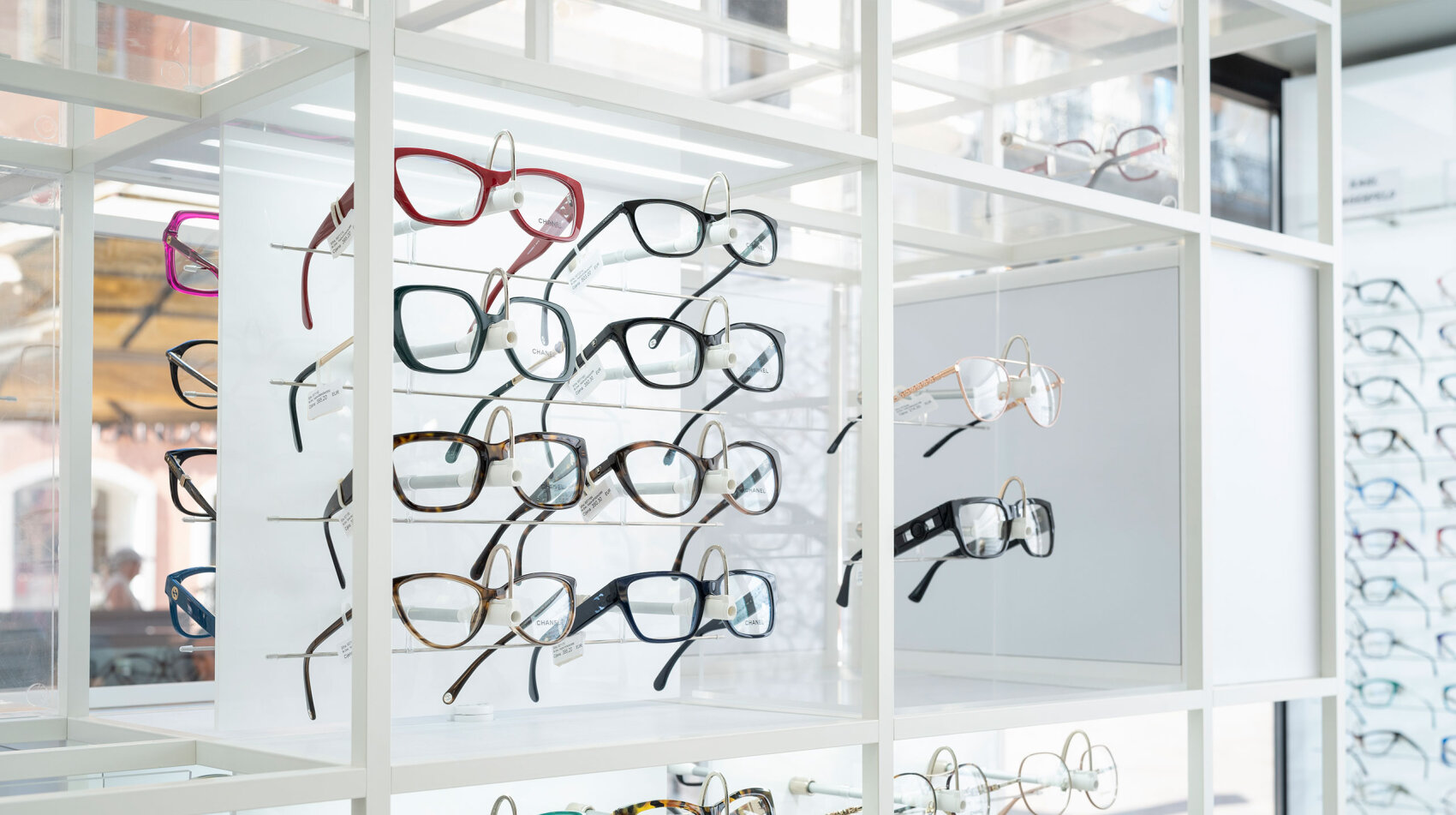 A display of various eyeglasses with different frame styles and colors arranged neatly on white shelves inside an optical store.