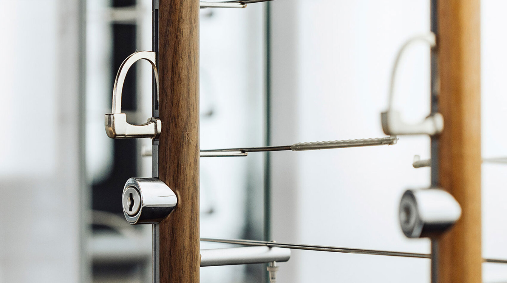 A close-up of metallic door handles and locks on glass doors, with blurred reflections and vertical wooden elements in the background. The image has a modern and minimalistic aesthetic.