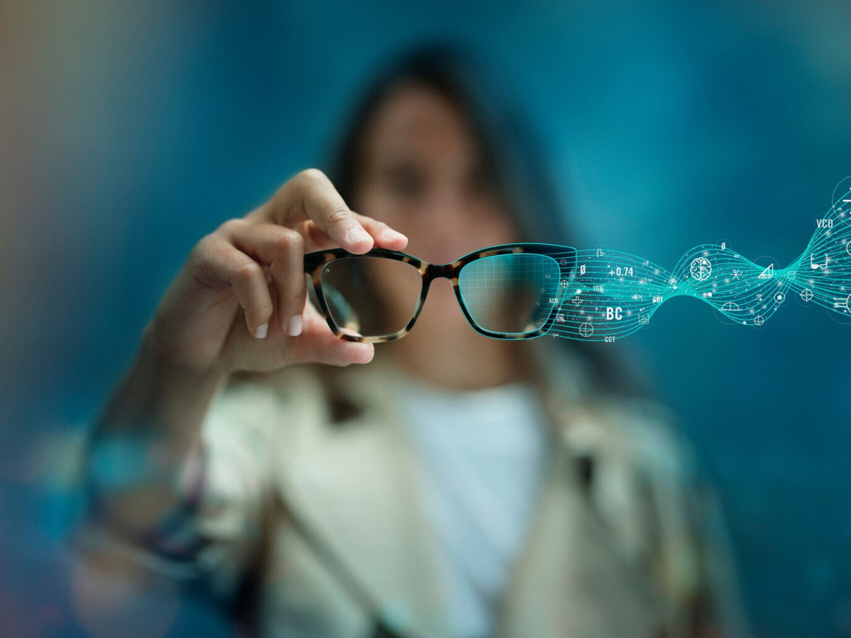 A person holds eyeglasses toward the camera as digital data and abstract symbols flow through the lenses, symbolizing advanced technology or augmented reality. The background is blurred and blue-toned.