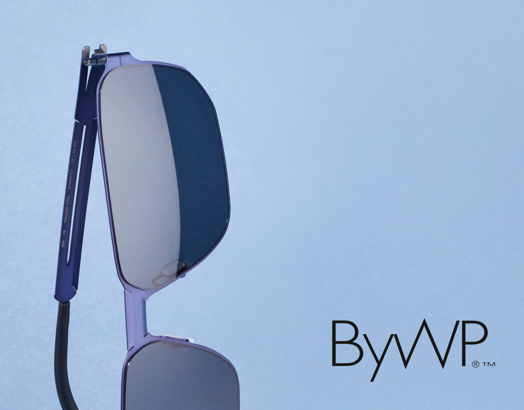 Eine moderne, geometrische Sonnenbrille mit dünnen, metallischen Rahmen ist vor einem hellblauen Hintergrund abgebildet. Das ByWP-Logo ist in der unteren rechten Ecke zu sehen.